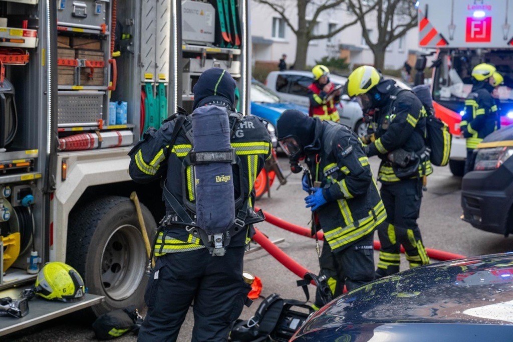 Drei Einsatzkräfte der Feuerwehr Leipzig stehen vor einem Feuerwehrfahrzeug und arbeiten. 