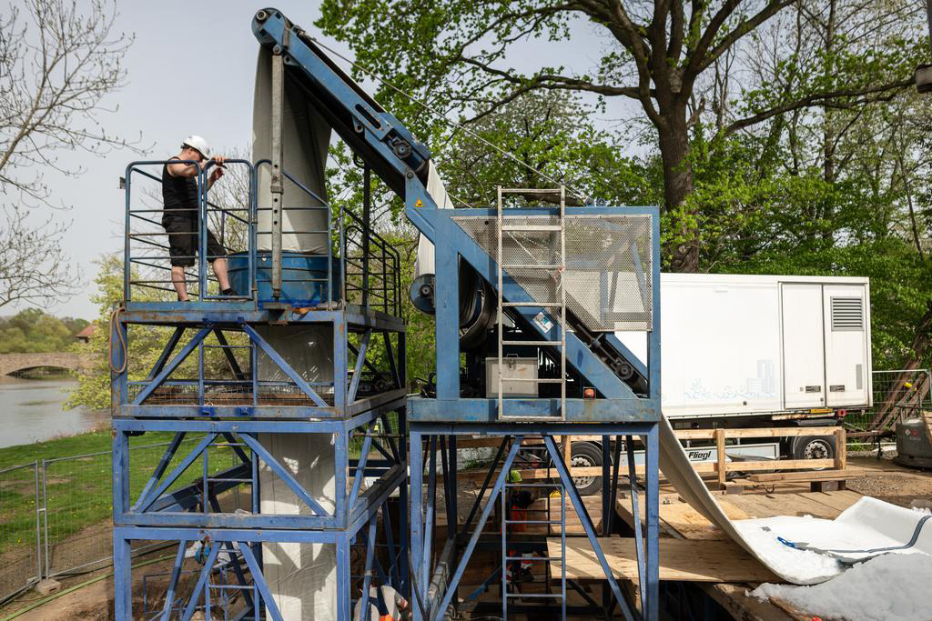 Über einen Förderturm wird ein großer Schlauch aus Gewebe in einen Abwasserkanal eingezogen. Auf dem Turm steht ein Arbeiter und kontrolliert den Vorgang. 
