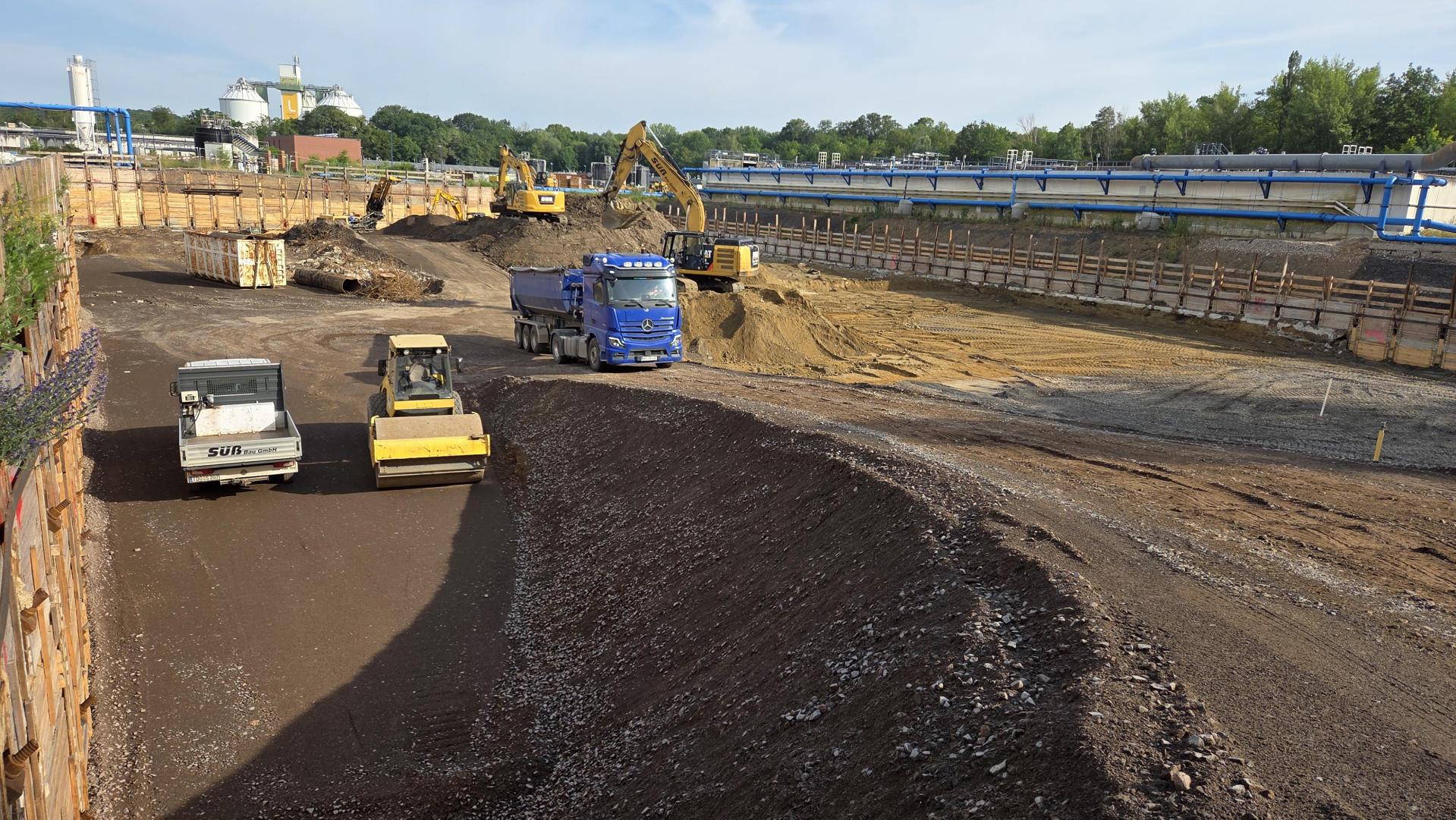 Mehrere Fahrzeuge und Bagger arbeiten in der riesigen Baugrube